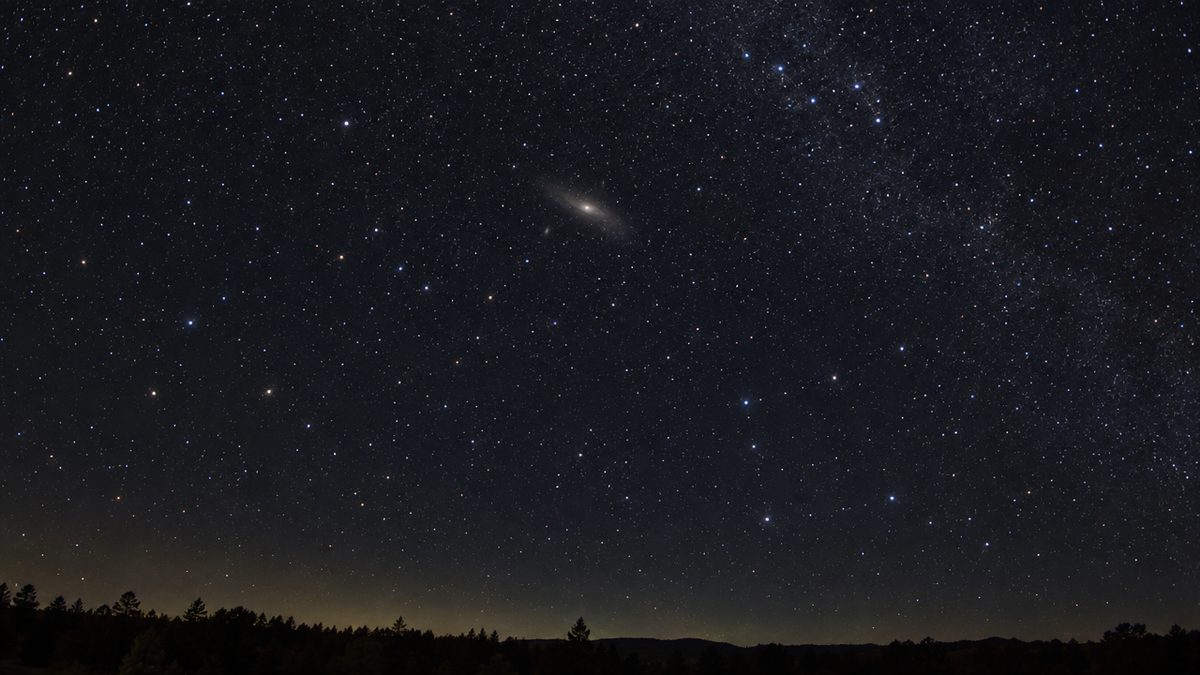 Illustration of the Andromeda Galaxy as a long, faint oval glow high in a dark autumn night sky