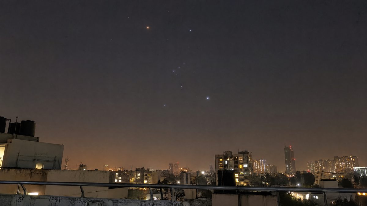 Illustration of a city rooftop at night under an orange-tinted sky, with Orion standing above the buildings